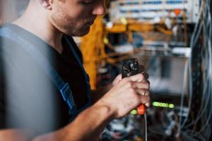 Young man in uniform works with internet equipment and wires in server room photo