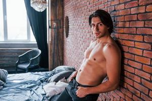 Shirtless sexy man leaning on the brick wall in bedroom at morning time photo