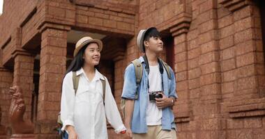 casal feliz viajante asiático com mão de chapéu juntos enquanto visitava o templo antigo. jovem sorridente e mulher andando e olhando o antigo templo. conceito de férias, viagens e hobby. video