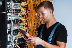 Young man in protective glasses works with internet equipment and wires in server room photo