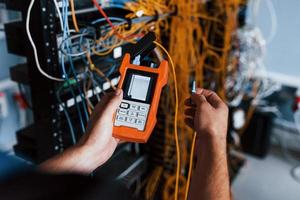 Young man withj measuring device in hands works with internet equipment and wires in server room photo