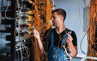 Young man in uniform feels confused and looking for a solution with internet equipment and wires in server room photo