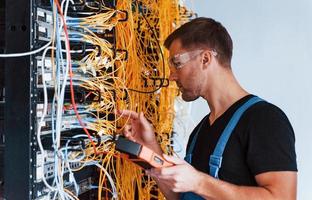 Young man in protective glasses works with internet equipment and wires in server room photo