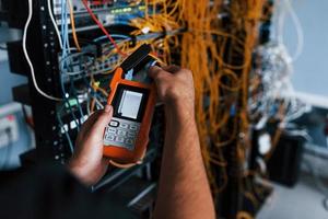 Young man withj measuring device in hands works with internet equipment and wires in server room photo