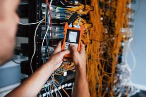 Young man withj measuring device in hands works with internet equipment and wires in server room photo