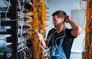 Young man in uniform feels confused and looking for a solution with internet equipment and wires in server room photo