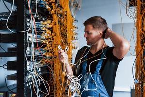 Young man in uniform feels confused and looking for a solution with internet equipment and wires in server room photo
