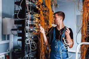 Young man in uniform feels confused and looking for a solution with internet equipment and wires in server room photo