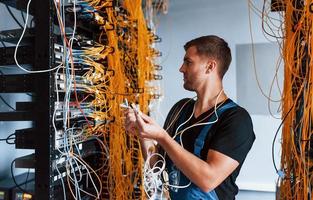 Young man in uniform feels confused and looking for a solution with internet equipment and wires in server room photo