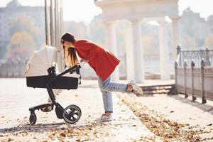 madre con abrigo rojo da un paseo con su hijo en el cochecito del parque en otoño foto