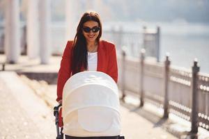 Mother in red coat have a walk with her kid in the pram in the park at autumn time photo