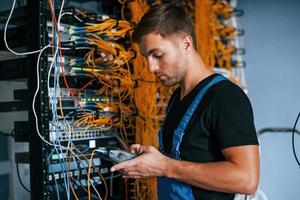 Young man in uniform have a job with internet equipment and wires in server room photo