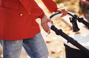 Close up view. Mother in red coat have a walk with her kid in the pram in the park at autumn time photo