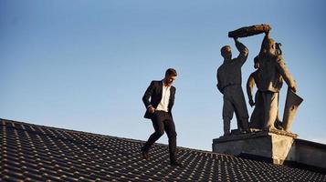 Man in black luxury clothes walk on the rooftop near the statue photo