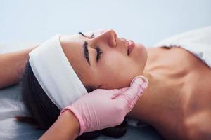 Close up view of woman that lying down in spa salon and have face cleaning procedure by cosmetologist in gloves photo