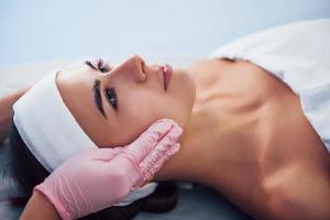 Close up view of woman that lying down in spa salon and have face cleaning procedure by cosmetologist in gloves