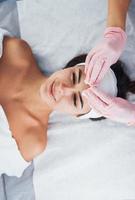 Close up view of woman that lying down in spa salon and have face cleaning procedure by cosmetologist in gloves photo