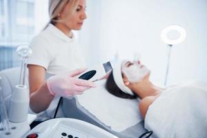 Woman lying down in spa salon and have face cleaning procedure by professional cosmetologist photo