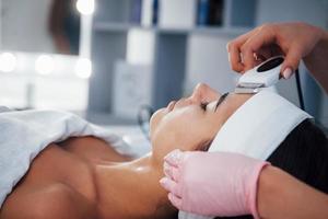 Using special device. Close up view of woman that lying down in spa salon and have face cleaning procedure photo