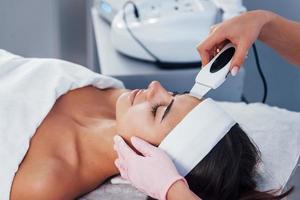 Using special device. Close up view of woman that lying down in spa salon and have face cleaning procedure photo