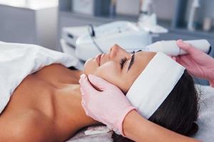 Close up view of woman that lying down in spa salon and have face cleaning procedure by using modern device photo