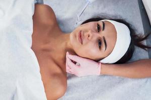 Close up view of woman that lying down in spa salon and have face cleaning procedure by cosmetologist in gloves photo