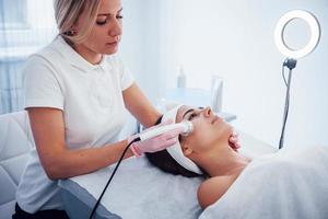 Woman lying down in spa salon and have face cleaning procedure by professional cosmetologist photo