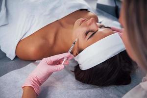 Close up view of woman that lying down in spa salon and have injection by the syringe into her face skin photo