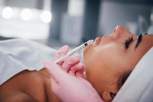 Close up view of woman that lying down in spa salon and have injection by the syringe into her face skin photo