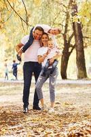 Mother and dad holds kids at shoulders and in hands. Cheerful young family have a walk in an autumn park together photo