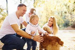 Cheerful young family with dog have a rest in an autumn park together photo