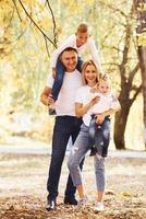 Mother and dad holds kids at shoulders and in hands. Cheerful young family have a walk in an autumn park together photo