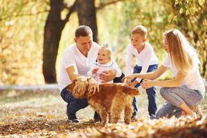 alegre familia joven con perro descansan juntos en un parque de otoño foto