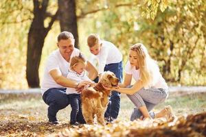 Cheerful young family with dog have a rest in an autumn park together photo