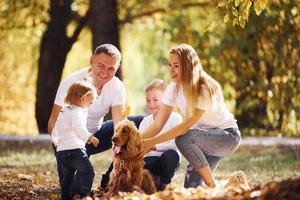 Cheerful young family with dog have a rest in an autumn park together photo