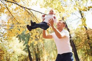 papá sostiene a su hija en las manos y se divierte en el parque de otoño foto