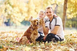 Dad with his daugher and dog have fun in an autumn park together photo