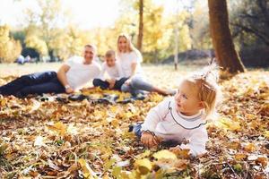 alegre familia joven tumbada en el suelo y descansando juntos en un parque de otoño foto