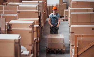 Young male worker in uniform is in the warehouse with pallet truck photo