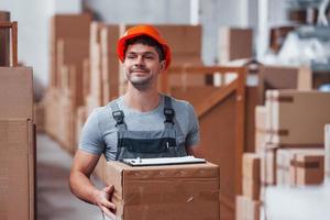 Worker in orange colored hard had is in storage with box in hands photo