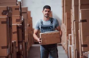 un joven trabajador uniformado está en el almacén con una caja en las manos foto