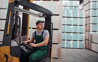 Young worker in unifrom sits in the forklift in the warehouse photo