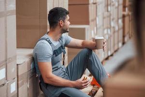 el trabajador de almacenamiento se sienta y toma un descanso. come sándwich y bebe café foto