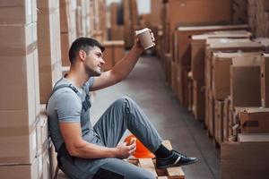 el trabajador de almacenamiento se sienta y toma un descanso. come sándwich y bebe café foto