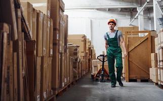 Young male worker in uniform is in the warehouse with pallet truck photo