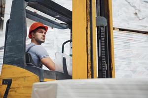 Young worker in unifrom sits in the forklift in the warehouse photo