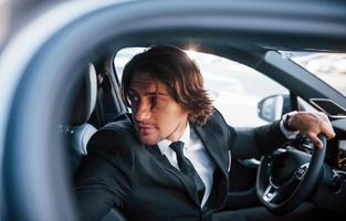 Young businessman in black suit and tie driving modern automobile photo