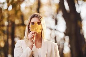 Portrait of young brunette with leaf that is in autumn forest at daytime photo