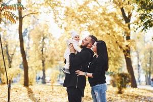 Cheerful family having fun together with their child in beautiful autumn park photo