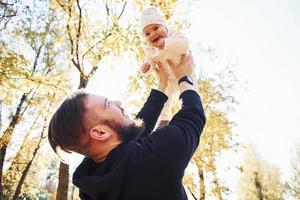 Nice sunlight. Father in casual clothes with his child is in the beautiful autumn park photo